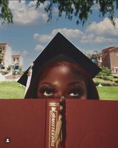 a woman wearing a graduation cap and gown peeking out from behind a red book