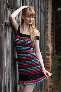 a woman leaning against a wooden fence wearing a colorful crochet dress and boots