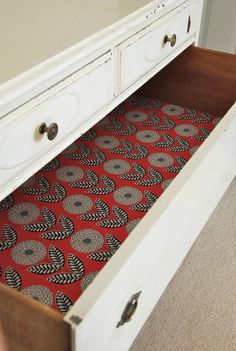 an open drawer with a red and black tie on it's bottom shelf in front of a white dresser