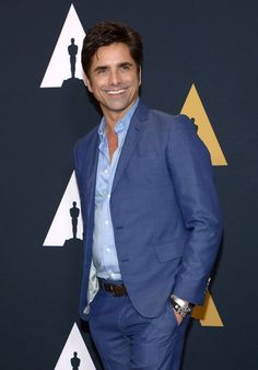 a smiling man in a blue suit stands on the red carpet at an oscars event