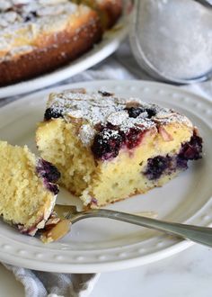 a slice of blueberry coffee cake on a white plate with a fork next to it