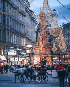 a horse drawn carriage on a city street with christmas lights hanging from the buildings behind it