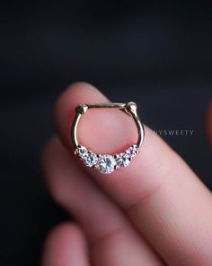 a close up of a person's hand holding an open nose ring with three stones