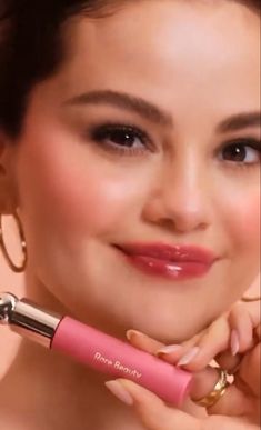 a woman holding a pink lipstick brush in her right hand and smiling at the camera