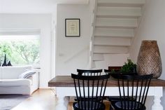 a dining room table with four chairs and a vase on top of it in front of the stairs