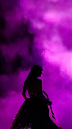 the silhouette of a woman in a long dress against a purple and black sky with clouds