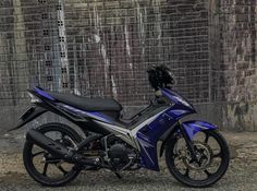 a blue and silver motorcycle parked in front of a brick wall with graffiti on it