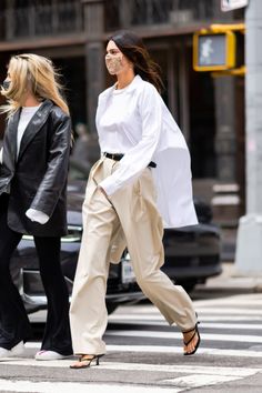 two women crossing the street in front of a car and one is wearing a white shirt