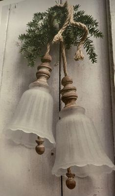 two bells hanging from the side of a building with pine needles on them and twine between them