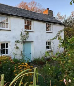 an old white house with blue door and windows surrounded by flowers in the foreground