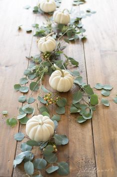 white pumpkins and greenery are arranged on the wooden floor, along with leaves