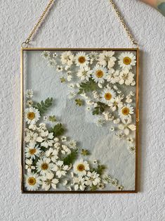 a frame hanging on the wall with daisies and leaves attached to it's sides