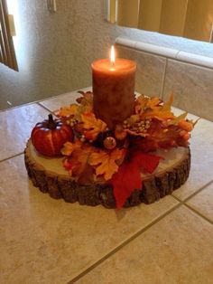 a candle that is sitting on top of a tree stump with leaves and pumpkins