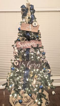 a decorated christmas tree with blue and white ornaments on it's top, sitting in front of a window