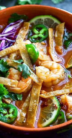 a bowl filled with shrimp and veggies on top of a table next to lime wedges