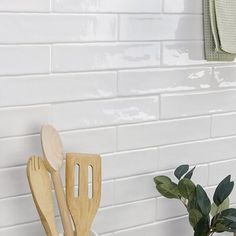 three wooden utensils and a potted plant in front of a white brick wall