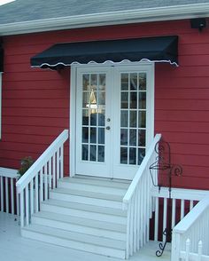 a red house with white stairs and a black awning over the front door that is open