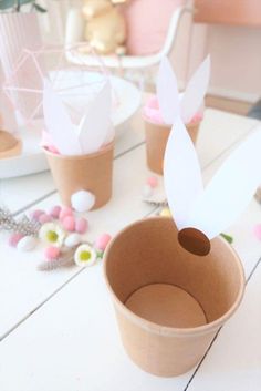 some paper birds are sitting in small cups on a table with flowers and other decorations