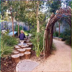 a woman is standing in the middle of a garden with trees and logs on the ground