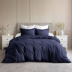 a bed with blue comforters and pillows in a white room next to two nightstands