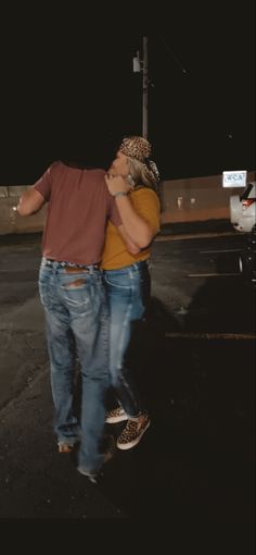 a man and woman walking down the street at night with their arms around each other