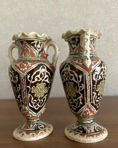 two vases sitting on top of a wooden table next to each other, with designs painted on them