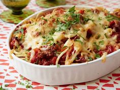 a casserole dish with meat, cheese and vegetables on a red and white tablecloth