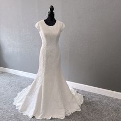 a white wedding dress is on display in a room with gray walls and carpeted flooring