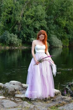 a woman in a dress standing on rocks by the water