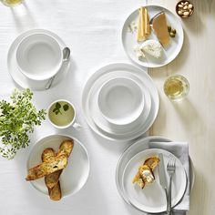 a table topped with white plates and bowls filled with different types of food next to utensils