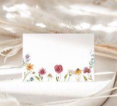 a white card with flowers on it sitting on a table next to feathers and other items