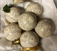 six decorative eggs with designs on them sitting on a sheet of white paper next to a gold ribbon