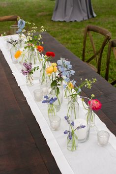 a long table with vases filled with flowers on top of it and candles in the middle