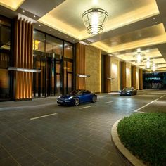 two cars are parked in front of a large building with lights on the side of it