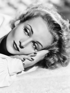 a woman laying on top of a bed with her hands under her chin and looking at the camera