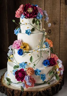 a multi - tiered wedding cake with colorful flowers on the top and bottom layer