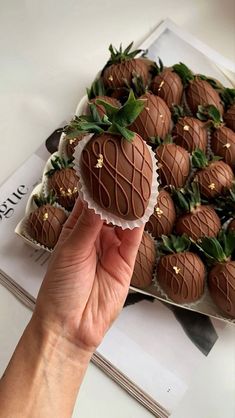 a hand holding a chocolate covered strawberries in front of a box of other chocolate covered strawberries