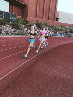 three women running on a track in front of a building