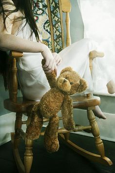 a woman sitting in a rocking chair holding a teddy bear