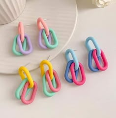 four pairs of multicolored earrings sitting on top of a white plate next to a flower