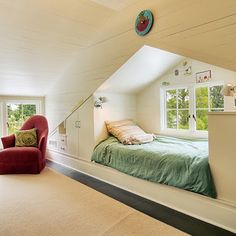 an attic bedroom with white walls and carpeted flooring, two red chairs in front of the bed