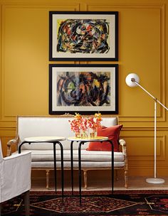 a living room with yellow walls and art on the wall, two chairs and a table