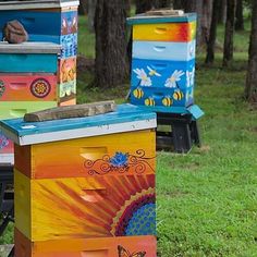 three beehives painted with different colors and designs in the grass next to trees