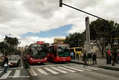 there are two red buses that are stopped at the crosswalk and people are waiting to get on