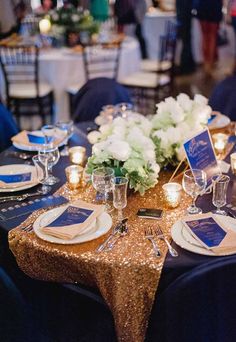 the table is set with gold sequins and blue napkins, silverware, and white flowers