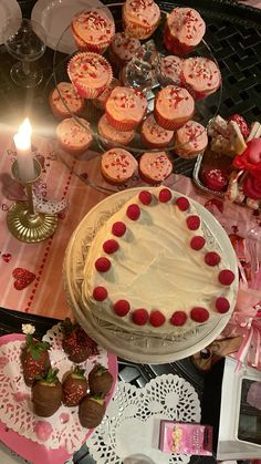 a table topped with cakes and cupcakes next to a lit candle