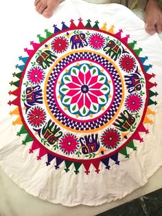 a person is holding up a colorful circular design on a white table cloth with an elephant and flower motif