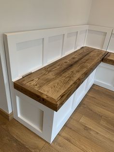 a wooden bench sitting on top of a hard wood floor next to a white wall