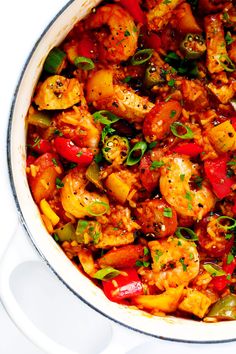 a pot filled with chicken and vegetables on top of a white countertop next to a wooden spoon