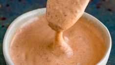 a wooden spoon in a white cup filled with brown liquid on top of a blue table